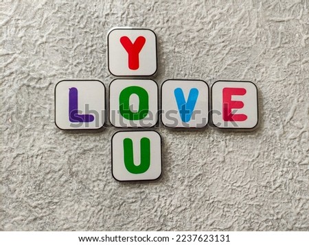 Crossword "LOVE YOU" of colorful magnetic plastics on gray textured background. Selective focus image