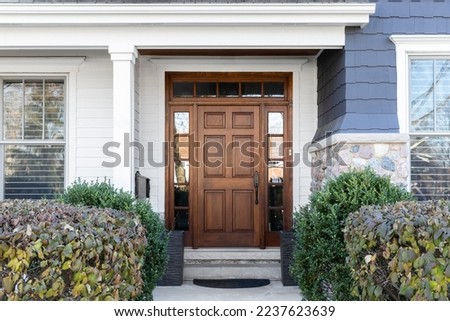 A wooden front door, surrounded by windows, with white, blue, and stone siding. Royalty-Free Stock Photo #2237623639