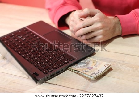 a bundle of Polish banknotes under a laptop and a person in a red sweatshirt