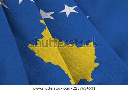 Kosovo flag with big folds waving close up under the studio light indoors. The official symbols and colors in fabric banner