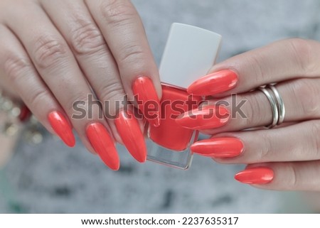 Woman hand with long nails and light orange neon manicure holds a bottle of nail polish	
