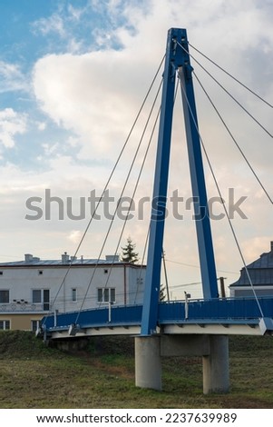 Suspension bridge for pedestrians on the Kamienna River (Stone River) in Ostrowiec Swietokrzyski.The span of the bridge hanging on steel suspension cables. Bridge pylon against the blue sky . Royalty-Free Stock Photo #2237639989
