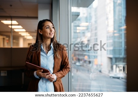 Young businesswoman holding digital tablet and day dreaming while looking through the window from her office. Copy space. Royalty-Free Stock Photo #2237655627
