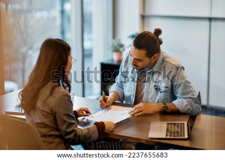 Hispanic man signing a contract while having meeting with financial advisor in the office.