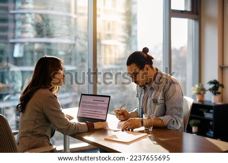 Asian human resource manager assisting young man in filling documents during job interview in the office. 
