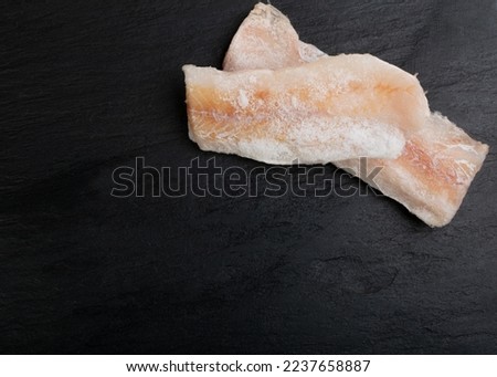 Frozen Fish on Black Plate, White Cod Fillet, Iced Hake Filet, Frozen Pollock Meat on Dark Background Top View