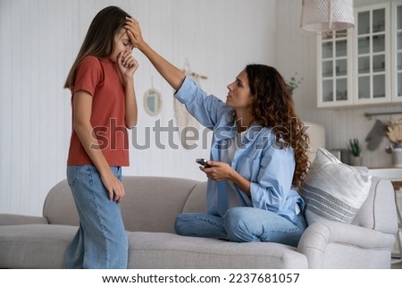 Worried mother holding mobile phone touching forehead of unhealthy coughing daughter, mom parent calling to doctor pediatrician, teen girl get sick, feeling unwell. Colds in children, caring for kids Royalty-Free Stock Photo #2237681057
