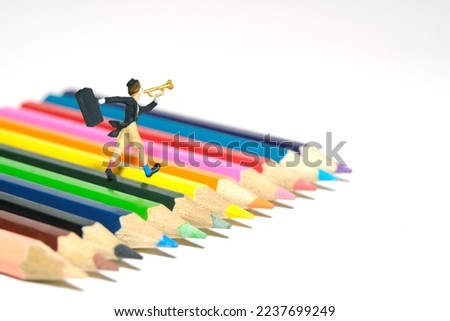 Miniature people toy figure photography. A clown wearing black suit and hat blow the trumpet walking above colored pencils. Isolated on white background. Image photo