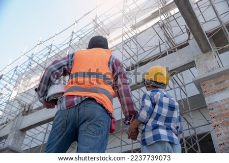 Male contractor holding boy's hand standing looking at building under construction, father taking son to look at his construction site, low view from behind, father and son holding hands. Royalty-Free Stock Photo #2237739073