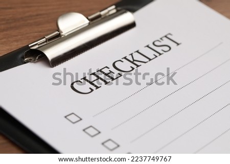 Clipboard with inscription Checklist on wooden table, closeup
