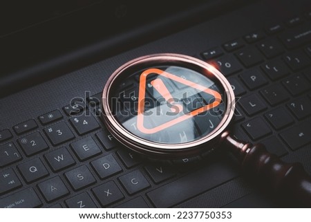 Magnifier glass with red triangle caution warning sign on laptop computer keyboard  for notification error and maintenance technology exclamation concept.