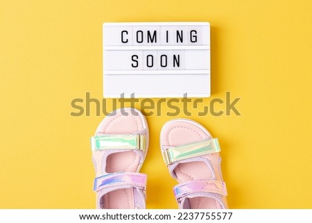 Coming soon. Motivational quote on lightbox and stylish holographic sandals on yellow background. Top view, Flat lay. Creative inspirational summer concept.