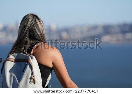 the girl with the backpack on her back looks towards the sea. photo during the day.