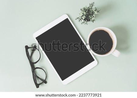 top view of white tablet with  glasses on planner, and blurred hot coffee cup on a light green background including copy space. For modern lifestyle communication, working space concept