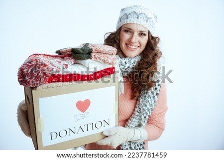Hello winter. smiling trendy woman in sweater, mittens, hat and scarf isolated on white background with donation box.