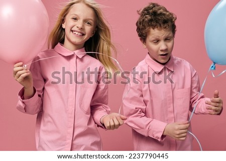 two happy cheerful children in pink shirts stand on a pink background and enjoy life with balloons in their hands