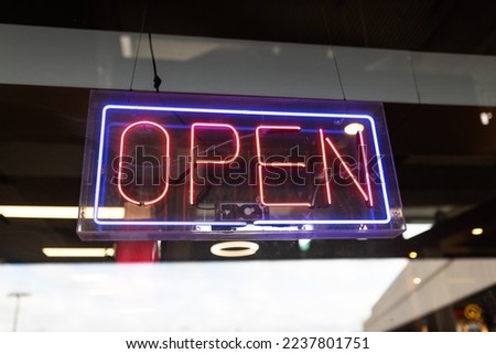 Open neon sign glowing in the dark on glass window. Colorful electric banner selective focus close up. Light bulbs radiance at night. Shiny illuminated lettering.