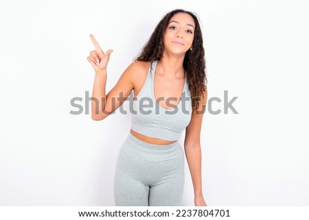 Beautiful teen girl with curly hair wearing gray sport set over white background pointing up with fingers number eight in Chinese sign language BÄ.
