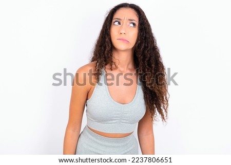 Beautiful teen girl with curly hair wearing gray sport set over white background making grimace and crazy face, screaming out of control, funny lunatic expressing freedom and wild.