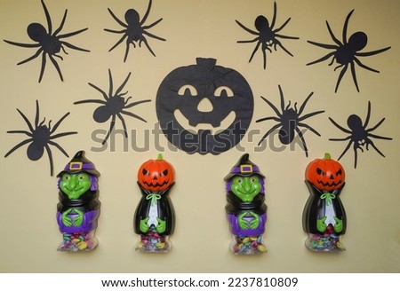 Cute characters in monster costume. Scary Halloween figurines stand on a light background close-up, behind hangs terrible black pumpkin. Halloween concept. Holiday decorations, toys and entertainment.
