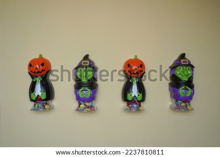 Cute character in monster costume. Scary Halloween figurines stand on a light background in close-up, behind hangs terrible pumpkin. Halloween concept. Holiday decorations and entertainment.