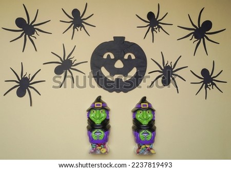 Cute witches in monster costume. Scary Halloween figurines stand on a light background close-up, behind hangs terrible black pumpkin. Halloween concept. Holiday decorations, toys and entertainment.