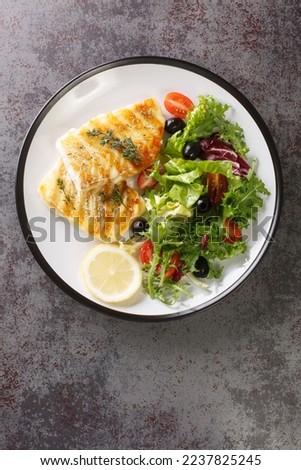 Grilled cod with fresh salad tomatoes, olives, lettuce mix close-up in a plate on the table. Vertical top view from above
