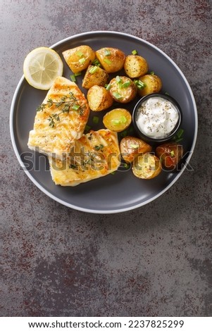 grilled cod fish with baked jacket potatoes, cream sauce and lemon close-up in a plate on the table. Vertical top view from above
