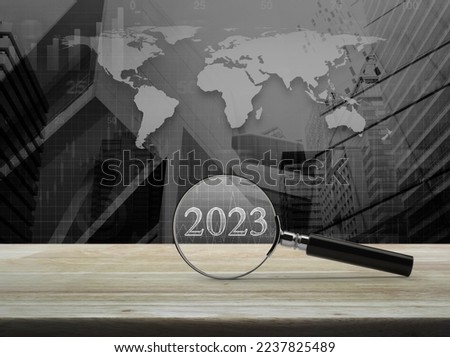 Magnifying glass with 2023 and financial graph on table over world map with city tower and skyscraper, Business happy new year 2023 research cover concept, Elements of this image furnished by NASA Royalty-Free Stock Photo #2237825489