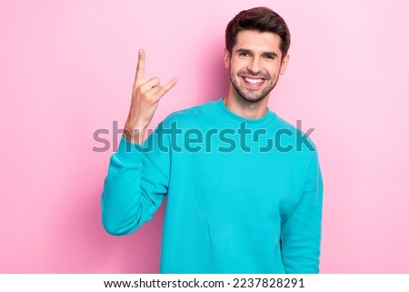 Photo of young positive cheerful handsome guy smiling enjoy his rock roll music album showing horned symbol fingers isolated on pink color background