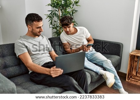 Two hispanic men couple using smartphone and laptop at home