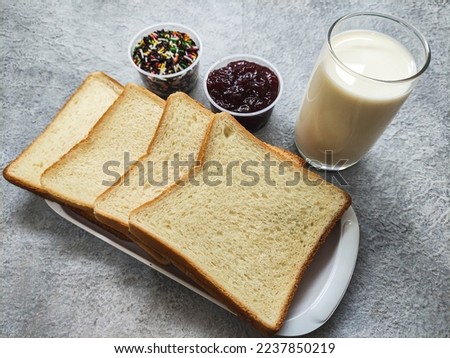 Simple breakfast set of white bread and milk completed with cup of chocolate sprinkles and jam