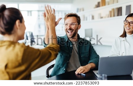 Successful business people giving each other a high five in a meeting. Two young business professionals celebrating teamwork in an office. Royalty-Free Stock Photo #2237853093