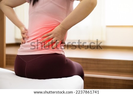 A woman sitting on a bed and holding her sore waist with her hand (the painful part is highlighted in red) Royalty-Free Stock Photo #2237861741