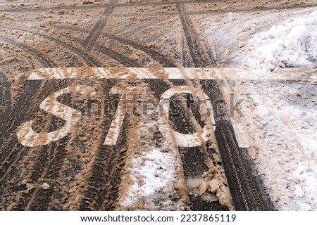 Winter road with STOP sign  and car tracks in dirty snow and de-icing chemicals.Danger driving in winter.