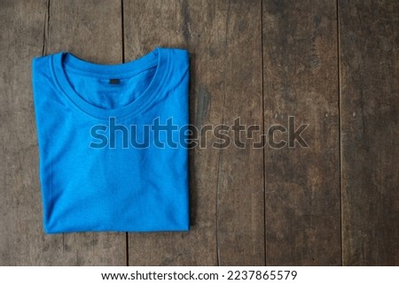 Folded blue t-shirt mockup over wooden background