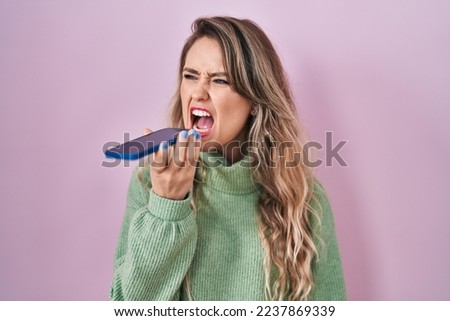 Young caucasian woman sending a voice message with smartphone angry and mad screaming frustrated and furious, shouting with anger. rage and aggressive concept.  Royalty-Free Stock Photo #2237869339