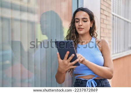 Young beautiful hispanic woman using touchpad at street