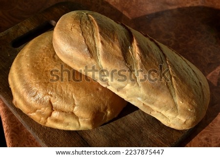 In the picture, two loaves of bread of different shapes lie on the kitchen table.