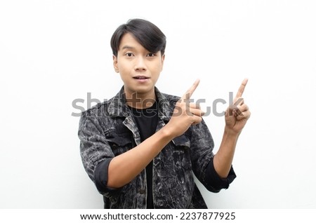 Happy Ecstatic asian man wear jacket jeans pointing finger to copy space presenting and showing goods. billboard model advertisment concept. man with wow face showing something. 