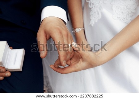 The hands of the bride in a white dress touch the ring on the hand of the groom in a dark blue suit
