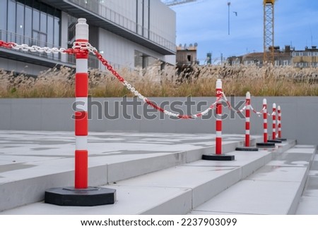 Bright orange traffic cones and plastic chain or car barriers. Side view of orange plastic street cones and poles with reflective silver tape near chain link fence at the entrance of a building.