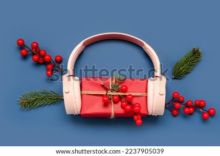 Headphones with Christmas gift, fir branches and cranberry on blue background