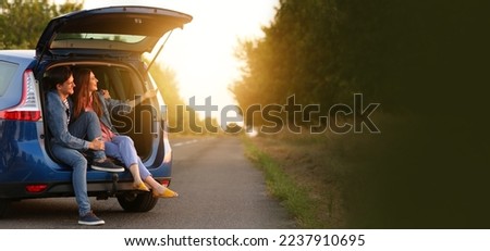 Happy couple sitting in trunk of their new car outdoors at sunset