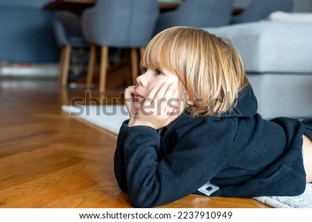 Close up portrait of cute blond child boy with pensive expression watching television at home.