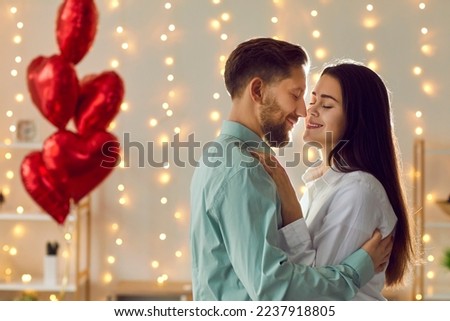 Happy loving couple celebrating St Valentine's Day. Young man and woman enjoying photosession as gift on Saint Valentine's Day, hugging, kissing, dancing in room with balloons and lights in background Royalty-Free Stock Photo #2237918805
