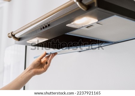 cropped shot of black metal hood extractor and person hand taking aluminum mesh filter on white wall background, maintenance household appliances Royalty-Free Stock Photo #2237921165
