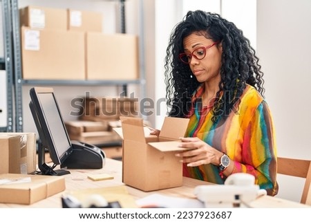 Middle age hispanic woman working at small business ecommerce looking inside box skeptic and nervous, frowning upset because of problem. negative person. 
