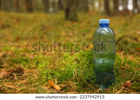 Plastic bottle of fresh water on ground in forest, space for text