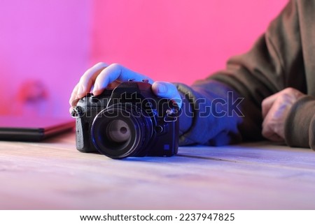 old digital SLR camera with the hand of a person in a green sweatshirt and a pink background